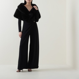 Model wearing Joseph Ribkoff Faux-Fur Collar Stole in black with rhinestone brooch, styled with black wide-leg jumpsuit and heeled sandals.