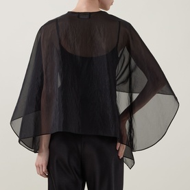 Model wearing Joseph Ribkoff Tie-Front Cover Up in black, semi-sheer shawl design with wide draped sleeves, styled over a black top and trousers.