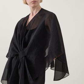Model wearing Joseph Ribkoff Tie-Front Cover Up in black, semi-sheer fabric with wide sleeves and front tie fastening, over black dress.