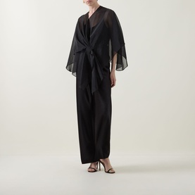 Model wearing Joseph Ribkoff Tie-Front Cover Up in black, semi-sheer fabric with flutter sleeves and tie-front detail, styled over black wide-leg