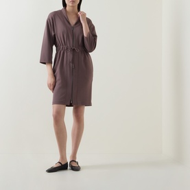 Model wearing a mauve zip-front mini dress with drawstring waist, three-quarter sleeves, and V-neckline, styled with black flat shoes.