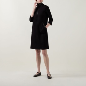 Model wearing Joseph Ribkoff black zip-front mock-neck dress with 3/4 sleeves and side pockets, styled with black Mary Jane flats.