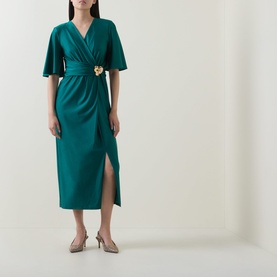 Model wearing Joseph Ribkoff Dress in Opulent Green with flutter sleeves, wrap front, gold floral belt detail, and front split, styled with nude