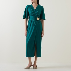 Model wearing Joseph Ribkoff Dress in Opulent Green, wrap-front midi style with flutter sleeves, gold floral belt detail, styled with nude heels.