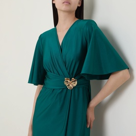 Model wearing Joseph Ribkoff Dress in Opulent Green with flutter sleeves, V-neckline, and gold heart-shaped waist buckle detail.