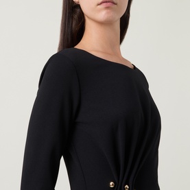Model wearing Joseph Ribkoff black dress with asymmetric neckline, long sleeves, and gold-tone button detail at hip.