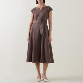 Model wearing Joseph Ribkoff Dress in Mink, featuring a V-notch neckline, cap sleeves, tie waist, and full midi skirt. Styled with white heels.