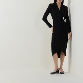 Model wearing Joseph Ribkoff black long-sleeve wrap dress with ruched skirt and silver pin detail, styled with black heeled flats.