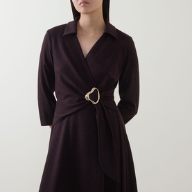 Model wearing dark burgundy wrap dress with V-neck collar, long sleeves, and gold horsebit buckle belt detail at waist