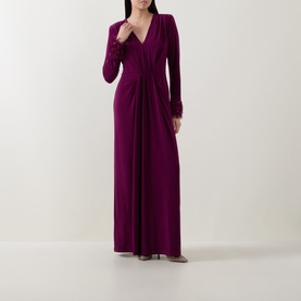 Model wearing a purple long-sleeve maxi dress with V-neckline, ruched waist detail and flowing skirt, styled with heeled sandals.