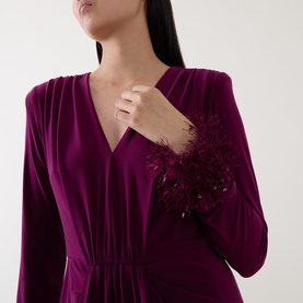 Model wearing a magenta long-sleeve V-neck dress with feather and sequin cuff embellishment, cinched waist detail visible.