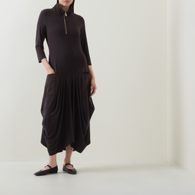 Model wearing Joseph Ribkoff Dress in Mocha, featuring zip-neck, three-quarter sleeves and draped drop-waist skirt, styled with black ballet flats.
