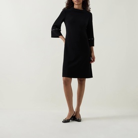 Model wearing Joseph Ribkoff Jewel Embellished Dress in black, midi-length shift silhouette with jewel-embellished flared cuffs and cropped sleeves