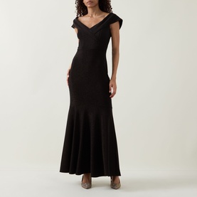 Model wearing Joseph Ribkoff bronze maxi dress with off-shoulder neckline, cap sleeves, and flared mermaid hem, styled with heeled mules.