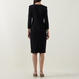 Model wearing Joseph Ribkoff Gathered Bow Pencil Dress in black, midi length, three-quarter sleeves, rear vent visible, styled with metallic heels.