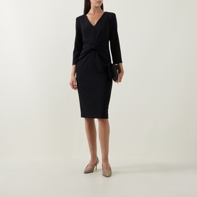 Model wearing Joseph Ribkoff Gathered Bow Pencil Dress in black, V-neck, three-quarter sleeves, styled with nude heels and black clutch bag.