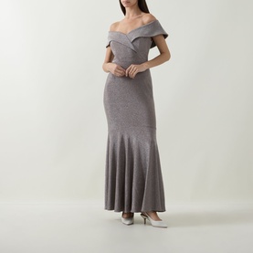 Model wearing Joseph Ribkoff Off-The-Shoulder Mermaid Dress in taupe lurex, maxi length with fitted silhouette and flared skirt. Styled with silver