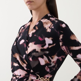 Model wearing Joseph Ribkoff Printed Wrap Dress in black/multi abstract print, showing V-neckline, long sleeves, and gold chain hardware detail.