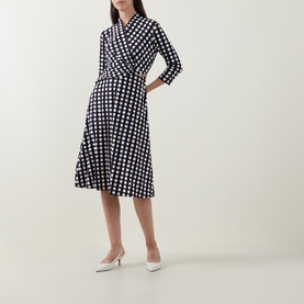 Model wearing Joseph Ribkoff Printed Wrap Dress in navy polka dot, midi length with flared skirt and three-quarter sleeves, styled with white