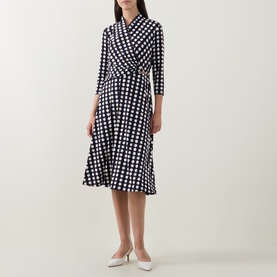 Model wearing Joseph Ribkoff Printed Wrap Dress in navy polka dot, three-quarter sleeves, flared midi skirt, styled with white heels.