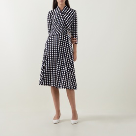 Model wearing Joseph Ribkoff Printed Wrap Dress in navy polka dot, three-quarter sleeves, flared midi skirt, styled with white heels.