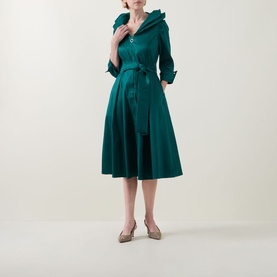 Model wearing Joseph Ribkoff Dress in Opulent Green with ruffle collar, belted waist, and full midi skirt, styled with nude flats.