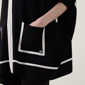 Model wearing Joseph Ribkoff Jacket in black with white contrast trim detailing on pockets and hem, hands in front pocket.