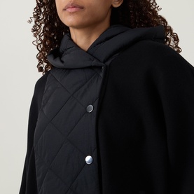 Model wearing Joseph Ribkoff black jacket with quilted front panel, silver snap buttons, and layered hoodie detail, close-up view.