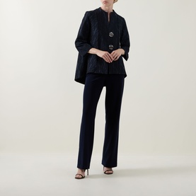 Model wearing Joseph Ribkoff navy quilted jacket with brooch detail, styled with matching navy trousers and black heeled sandals.