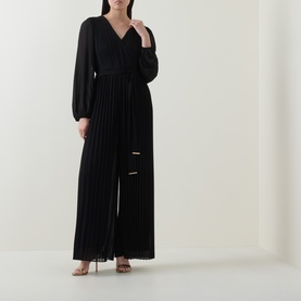 Model wearing Joseph Ribkoff black pleated wide-leg jumpsuit with wrap V-neckline and long balloon sleeves, styled with strappy heels.