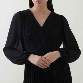 Model wearing Joseph Ribkoff black jumpsuit with V-neckline, pleated bodice, and sheer long sleeves in 100% polyester.