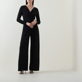Model wearing Joseph Ribkoff black jumpsuit with wrap-style V-neckline, long sleeves, and wide-leg trousers, styled with strappy heels.
