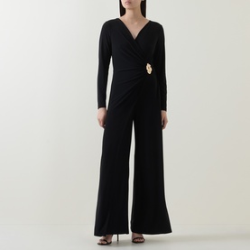 Model wearing Joseph Ribkoff black jumpsuit with wrap-style V-neckline, long sleeves, gold brooch detail, and wide-leg trousers.