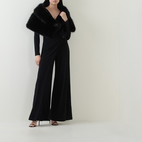 Model wearing Joseph Ribkoff black wide-leg jumpsuit with wrap-style top, styled with a black faux fur stole and strappy heels.