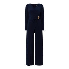 Joseph Ribkoff Midnight Blue jumpsuit with long sleeves, wrap-style ruched waist, gold brooch detail, and wide-leg trousers