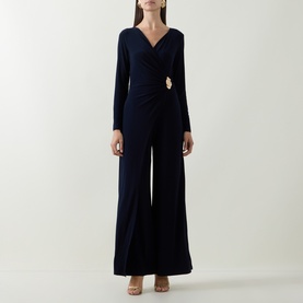 Model wearing Joseph Ribkoff Midnight Blue jumpsuit with wrap V-neckline, gold buckle detail, long sleeves and wide-leg trousers.