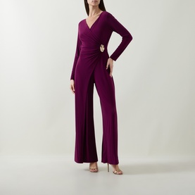 Model wearing Joseph Ribkoff Berry Burst jumpsuit with wrap-style V-neck, long sleeves, gold brooch detail, and wide-leg trousers