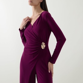 Model wearing Joseph Ribkoff Berry Burst jumpsuit with wrap-style V-neckline, ruched waist, gold brooch detail, and long sleeves.