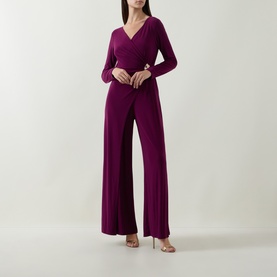 Model wearing Joseph Ribkoff Berry Burst jumpsuit with wrap-style bodice, long sleeves, wide-leg trousers and gold-tone buckle waist detail.