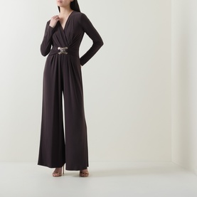 Model wearing Joseph Ribkoff Jumpsuit in Mocha, wide-leg silhouette with V-neckline, long sleeves, and embellished waist detail, styled with strappy