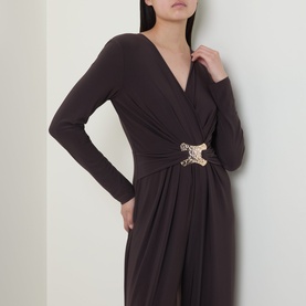 Model wearing Joseph Ribkoff Jumpsuit in Mocha, featuring a wrap-style V-neck, long sleeves, and gold ornamental waist clasp with draped detail.