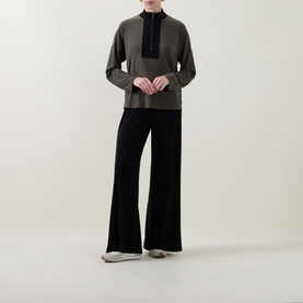 Model wearing Joseph Ribkoff Top in Avocado/Black with half-zip bib detail, styled with wide-leg black trousers and white trainers.
