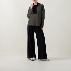 Model wearing Joseph Ribkoff Top in Avocado and Black with contrast panel neckline, styled with wide-leg black trousers and grey flat shoes.