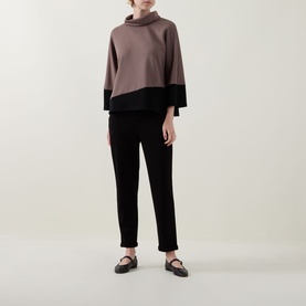 Model wearing Joseph Ribkoff Mink and Black colour-block turtleneck top with wide sleeves, styled with black slim-fit trousers and flat shoes.