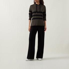 Model wearing Joseph Ribkoff Striped Hoodie in avocado and black with asymmetric hem and side slits, styled with wide-leg black trousers.