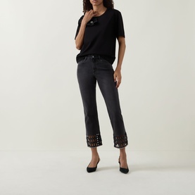 Model wearing Joseph Ribkoff black short-sleeve top, styled with dark cropped jeans featuring laser-cut hem detail and black heels.