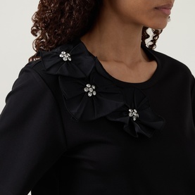 Model wearing Joseph Ribkoff black top with ruffled neckline detail and crystal flower embellishments, close-up view