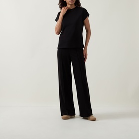Model wearing Joseph Ribkoff black short-sleeve top with subtle shoulder detail, styled with wide-leg black trousers and nude flats.