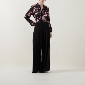 Model wearing Joseph Ribkoff Black/Multi floral print blouse with tie neck, styled with wide-leg black trousers.