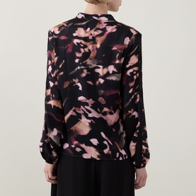 Model wearing Joseph Ribkoff Top in black multicolour abstract floral print, long sleeves with pintuck detail, back view, paired with black trousers.